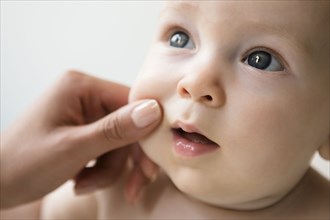 Hand of mother pinching cheek of baby son