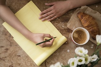 Hispanic woman writing on yellow notepad at breakfast