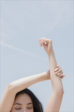 Hispanic woman stretching arms under blue sky