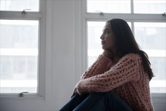 Hispanic woman wearing pink sweater and jeans near window
