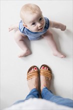 Caucasian baby boy sitting on floor at feet of mother
