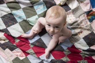 Caucasian baby boy sitting on blanket looking up