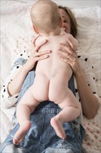 Caucasian mother laying on bed holding naked baby son