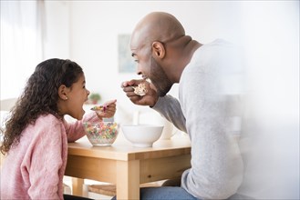 Father and daughter eating cereal at table