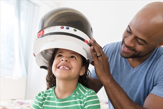 Father placing astronaut helmet on daughter