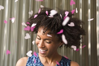 Heart-shape confetti falling on smiling Black woman