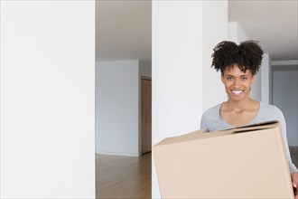 Black woman carrying cardboard box in empty apartment