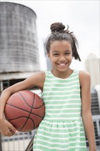 Mixed Race girl holding basketball in city