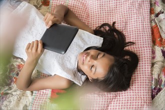Mixed Race girl laying on bed using digital tablet