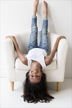 Mixed Race girl laying upside-down on armchair