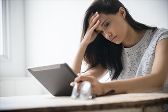 Mixed Race woman with headache using digital tablet