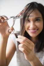 Mixed Race woman cutting hair with scissors