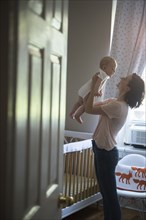 Caucasian mother holding baby son face to face in bedroom
