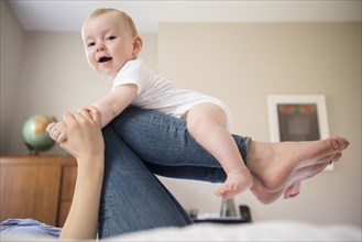 Caucasian mother laying on bed balancing baby son on legs