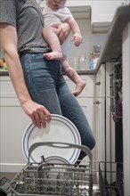Caucasian mother holding baby son holding plate in dishwasher