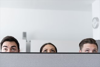 Eyes of business people looking up over cubicle wall in office