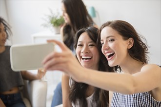Smiling women posing for cell phone selfie at party