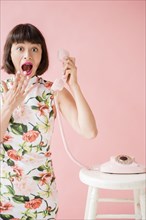 Surprised Hispanic woman wearing floral dress holding pink telephone
