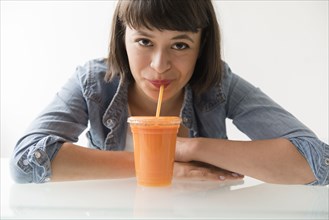 Hispanic woman drinking orange smoothie with straw