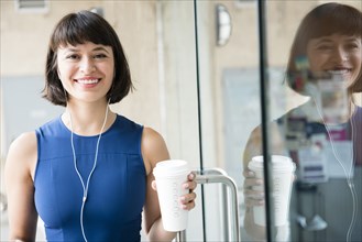 Hispanic woman drinking coffee and listening to earbuds