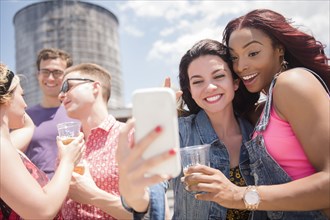 Smiling friends posing for cell phone selfie outdoors