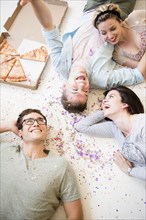Caucasian friends laying on floor with pizza and confetti