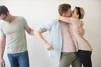 Caucasian man pulling arm of friend kissing girlfriend