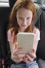 Smiling Caucasian girl texting on cell phone in car