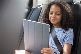 Smiling Hispanic girl using digital tablet in car