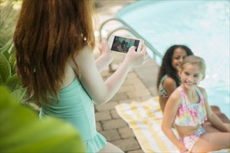 Girl photographing friends with cell phone at swimming pool