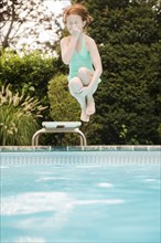 Caucasian girl holding nose jumping off diving board into swimming pool