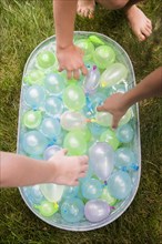 Hands of girls reach for water balloons in tub