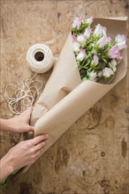 Hands of Caucasian woman wrapping bouquet in brown paper