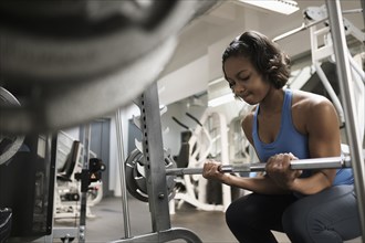 Mixed Race woman lifting barbell at gymnasium