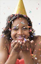 Mixed Race woman wearing party hat blowing confetti