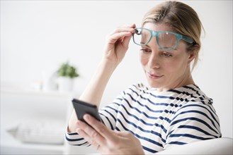 Caucasian woman lifting eyeglasses reading cell phone
