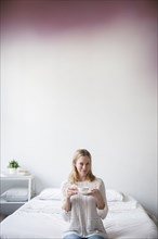 Portrait of Caucasian woman sitting on bed drinking tea