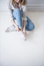 Caucasian woman sitting on floor tying shoelace
