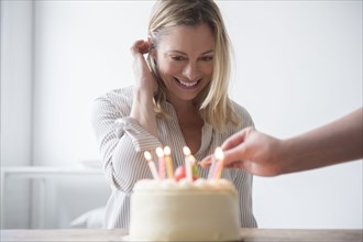 Friend lighting candles on birthday cake for Caucasian woman