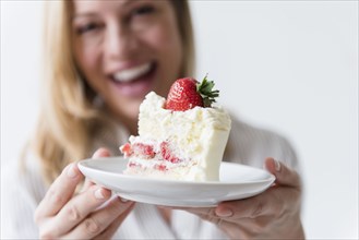 Caucasian woman holding slice on vanilla cake with strawberry