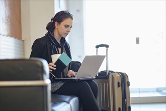 Hispanic woman holding passport using laptop in airport