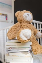 Teddy bear on stack of books near crib