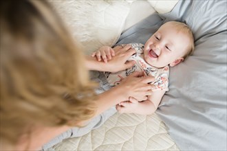 Caucasian mother tickling baby son on bed