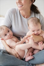 Caucasian mother holding twin baby daughters in lap