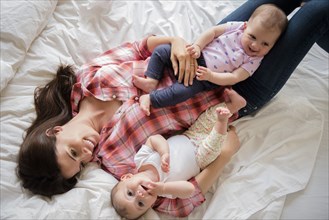 Caucasian mother laying on bed with twin baby daughters
