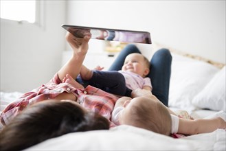 Caucasian mother on bed with twin baby daughters using digital tablet