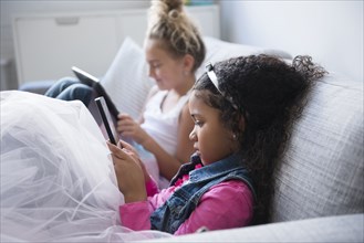 Girls using digital tablets on sofa