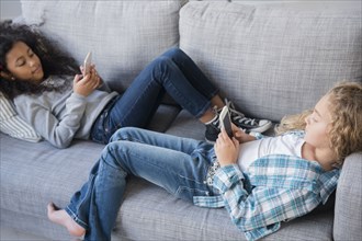 Girls laying on sofa texting on cell phones