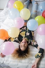 Mixed Race woman laying on bed covered with balloons