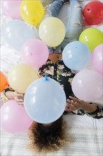 Mixed Race woman sitting on bed covered with balloons